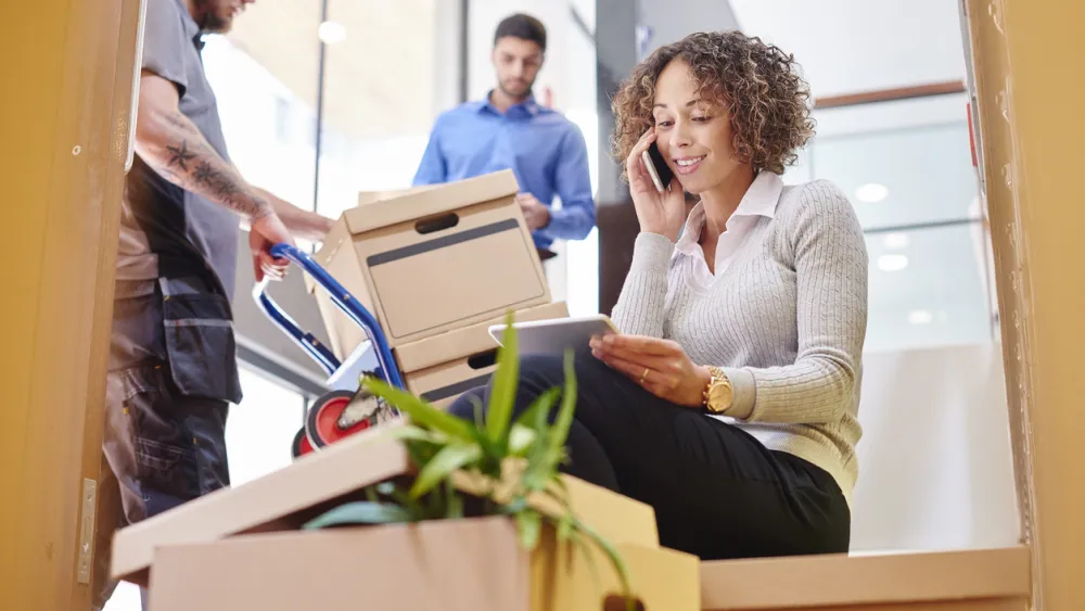 Mujer con expresión preocupada sentada en escaleras rodeada de cajas