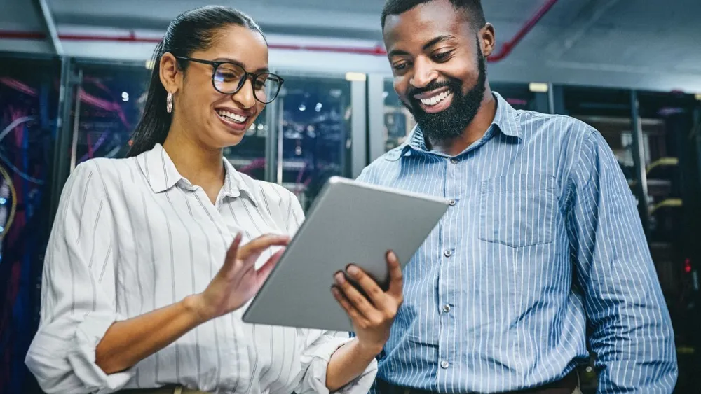Two colleagues smiling and reviewing a tablet in an office space