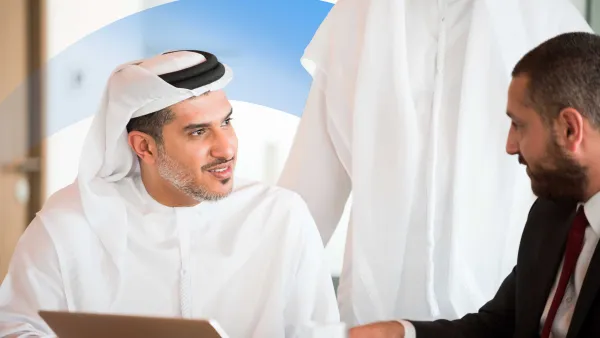 Businessman in traditional Middle Eastern attire meeting with a colleague and discussing work over coffee and a laptop.