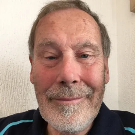 Close-up of a smiling elderly man with gray hair and beard against a light wall