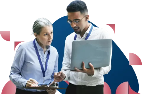 Two professionals in business attire reviewing a laptop together, with one wearing a lanyard badge
