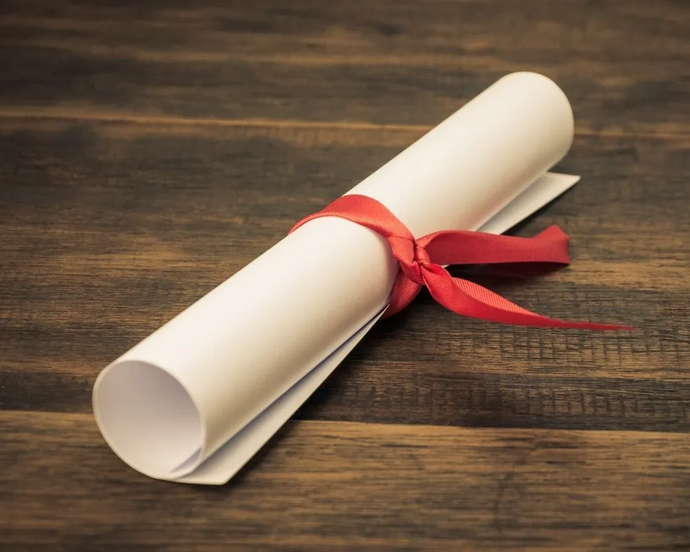Rolled paper scroll tied with red ribbon on dark wooden surface