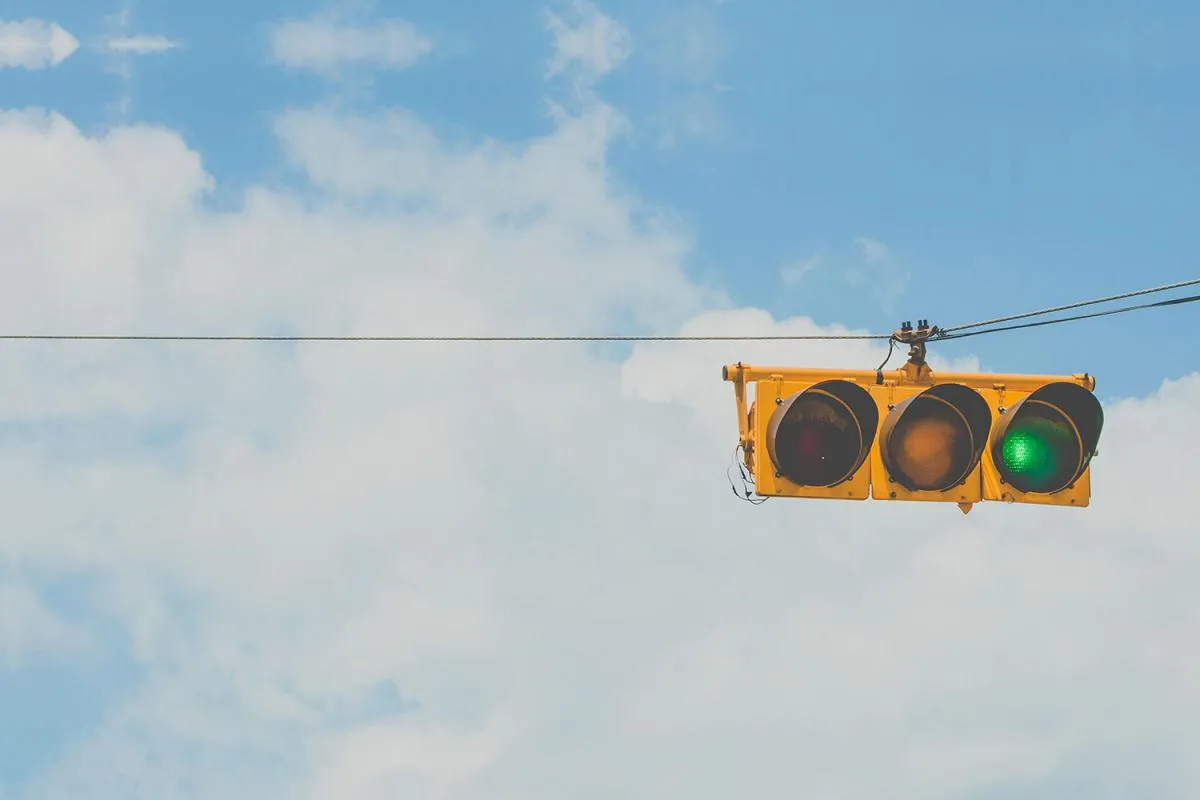 Yellow traffic light against blue cloudy sky. Green light is on signalling "Go"