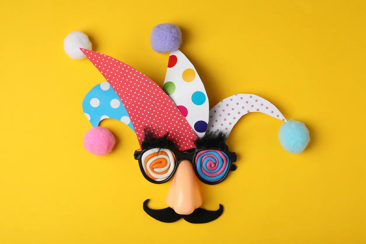Colorful carnival mask with fake mustache, glasses and pom-poms against a bright yellow background