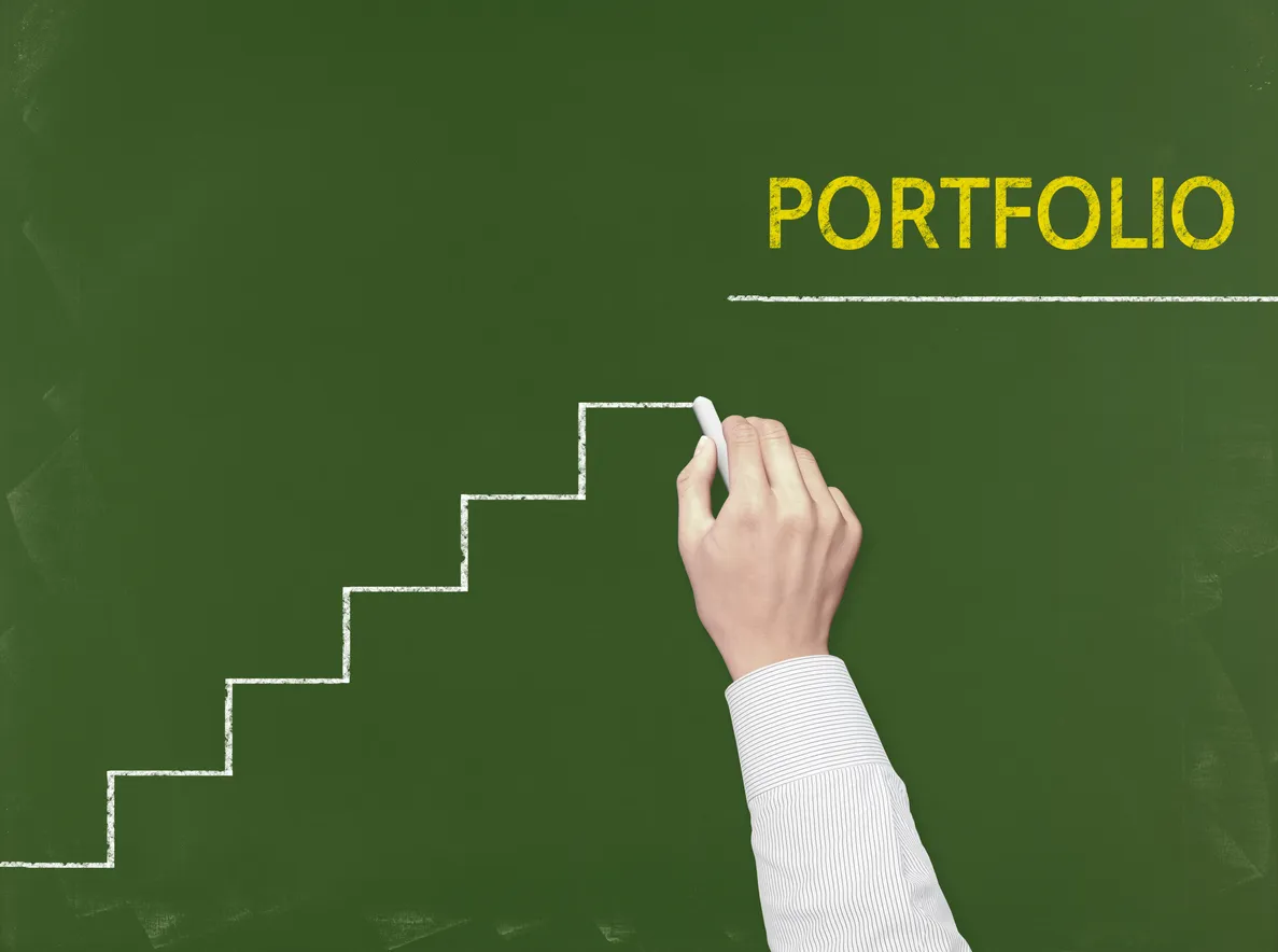 Hand writing 'Portfolio' with chalk on green chalkboard, with ascending staircase lines drawn beneath