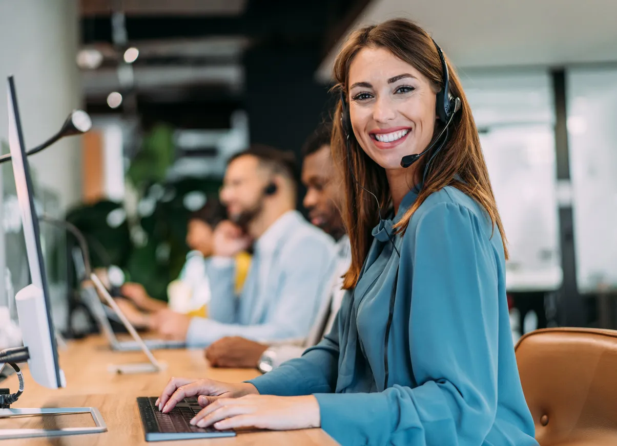 Customer service representative in blue blosue with headset working at computer in office setting