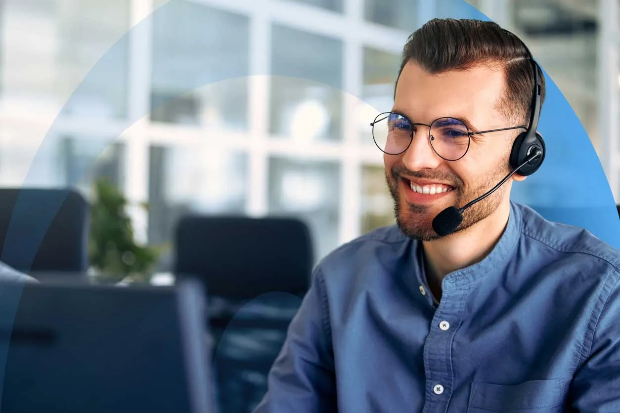 Smiling professional wearing a headset, looking at a computer monitor.