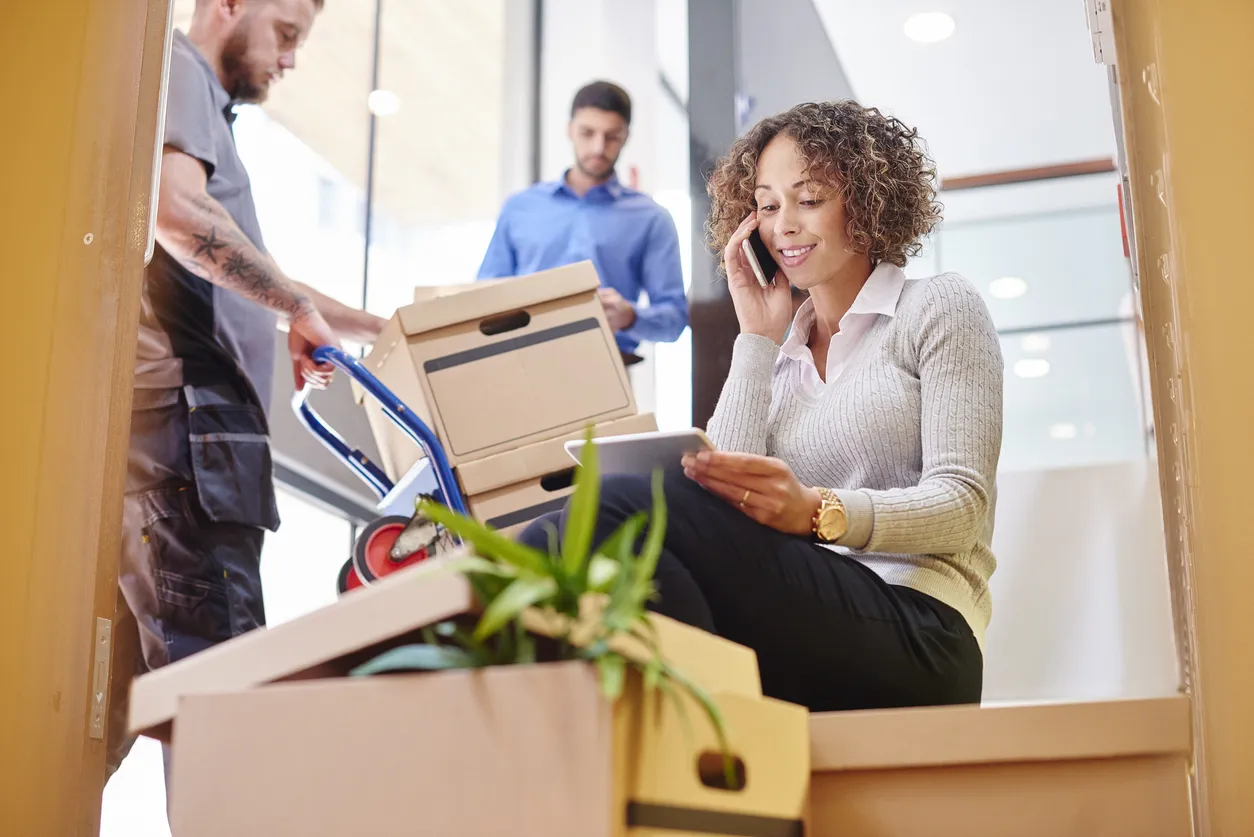 Mujer con expresión preocupada sentada en escaleras rodeada de cajas