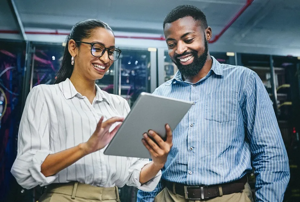 Two colleagues smiling and reviewing a tablet in an office space