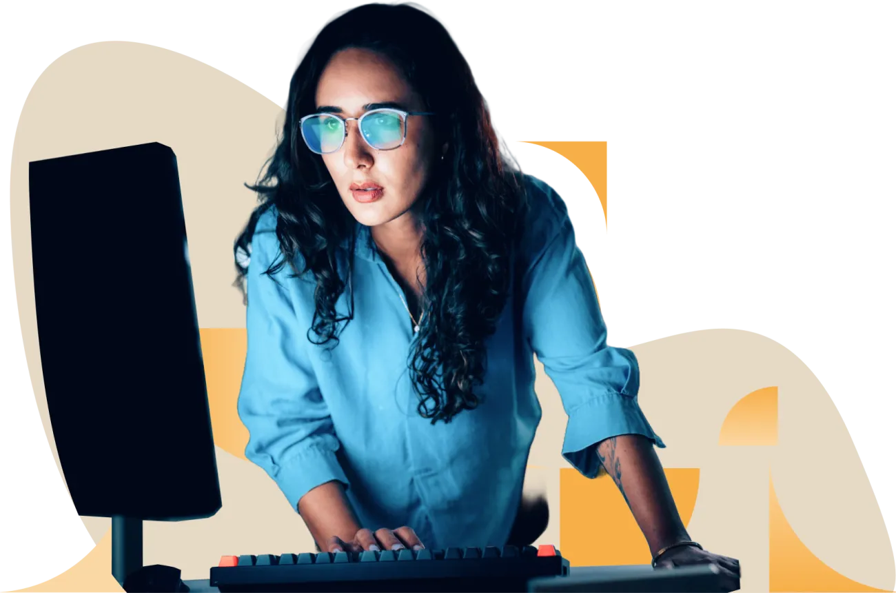 Woman with long dark hair wearing blue shirt and glasses, sitting at desk with computer monitor
