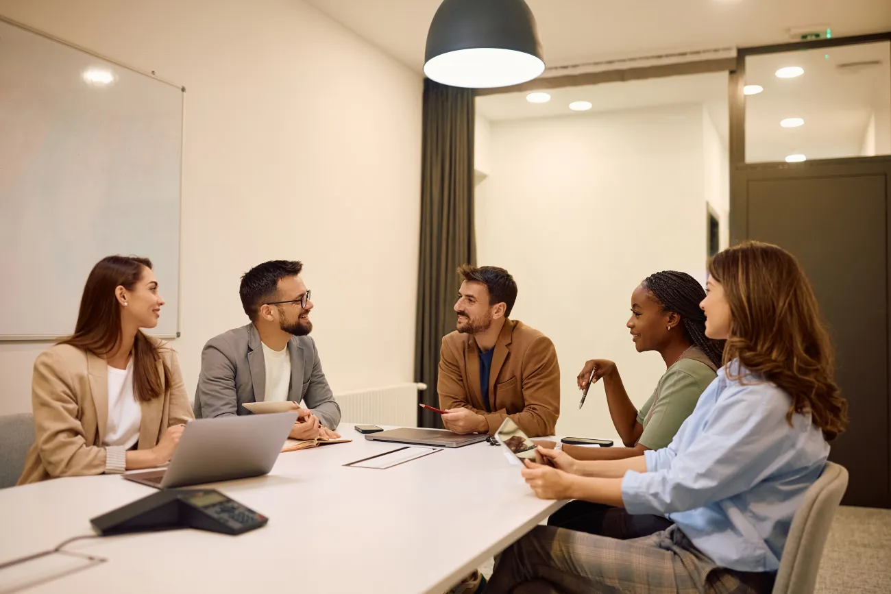 Five professionals sitting around a conference table during a meeting discussion.