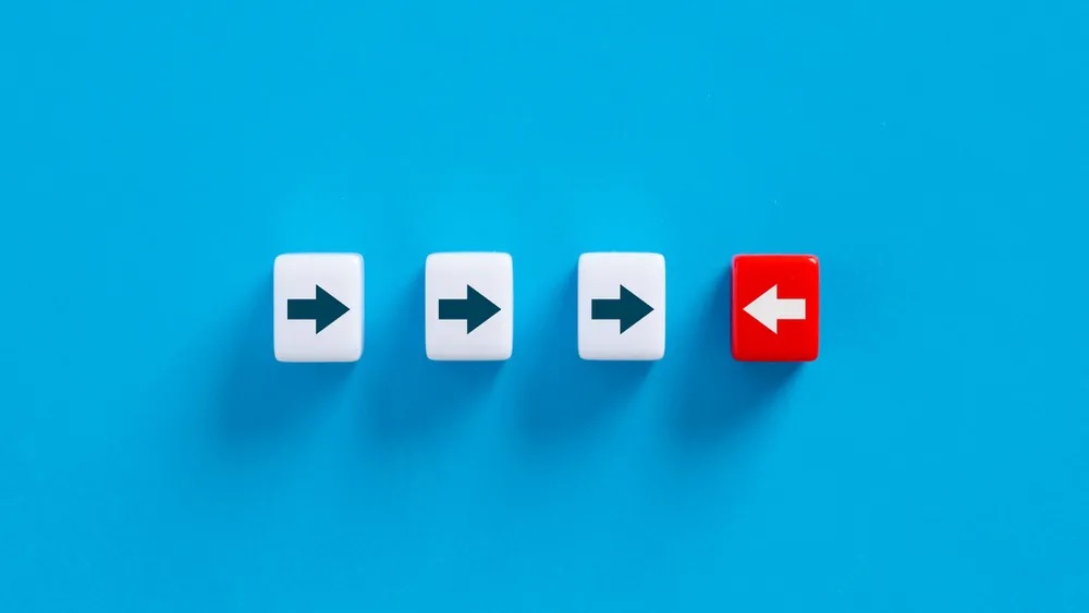 Three white forward arrows and one red backward arrow on bright blue background symbolizing resistance to change