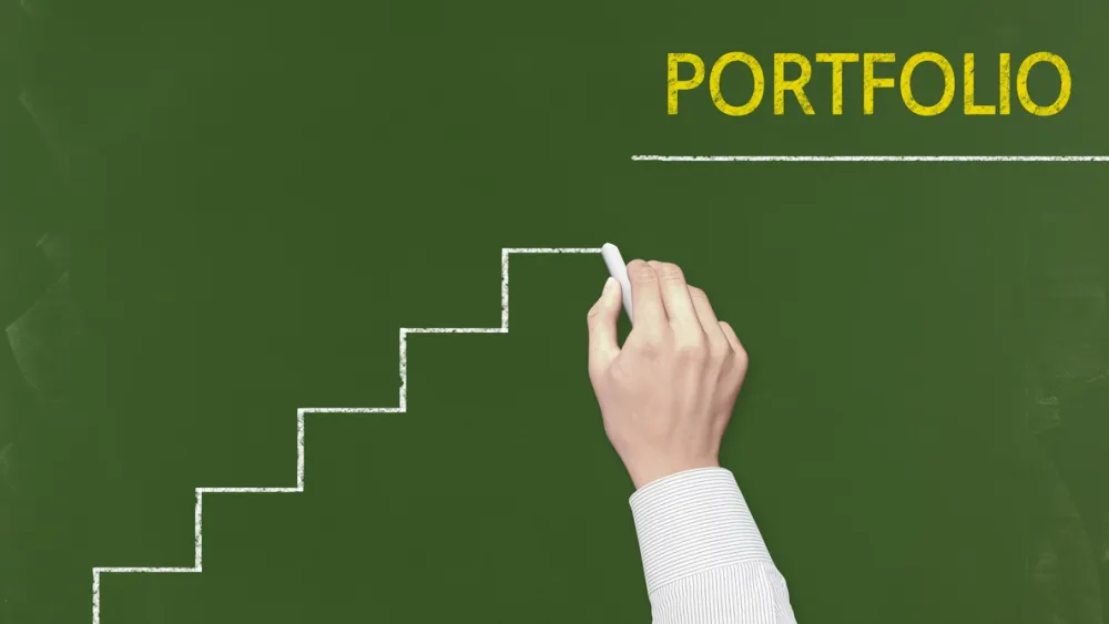 Hand writing 'Portfolio' with chalk on green chalkboard, with ascending staircase lines drawn beneath