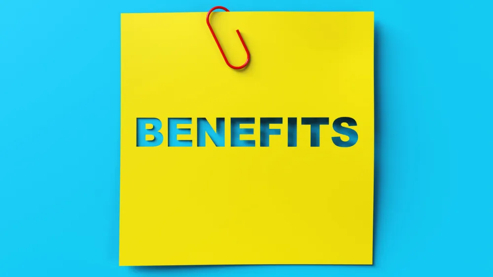 Yellow sticky note with BENEFITS text cut out attached with red paperclip on blue background