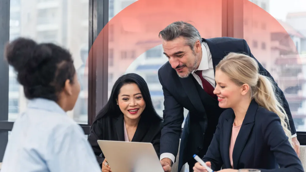 Diverse business team gathered around laptop, smiling and collaborating in modern office setting