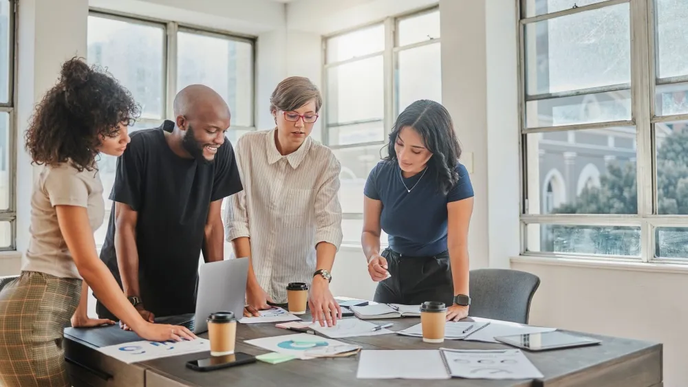 Four diverse professionals collaborating around a desk with documents and laptop in a bright office