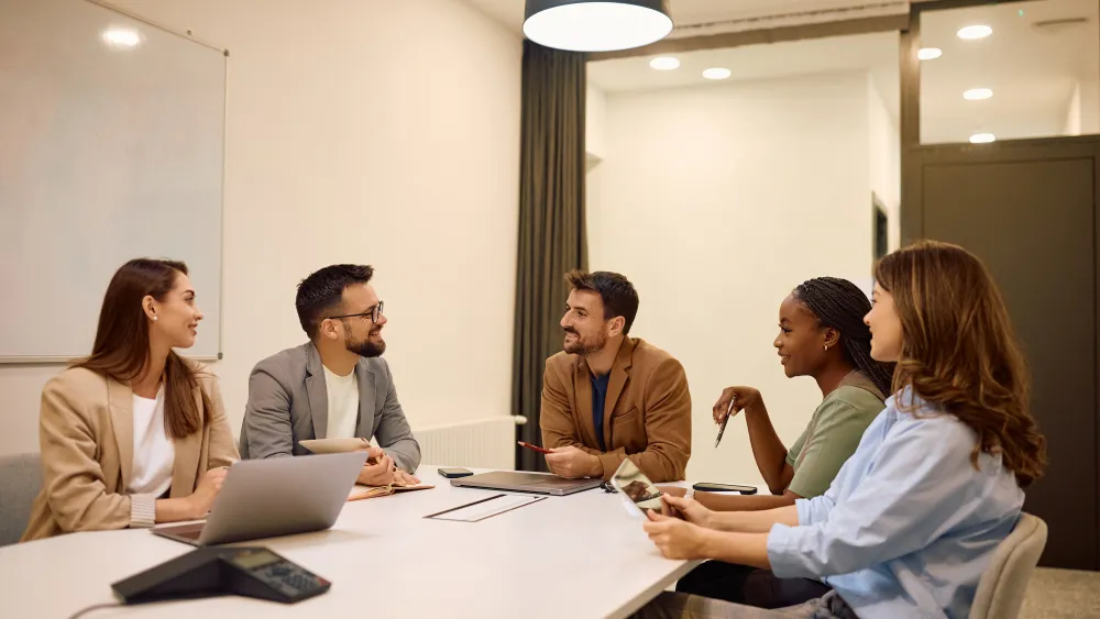 Five professionals sitting around a conference table during a meeting discussion.