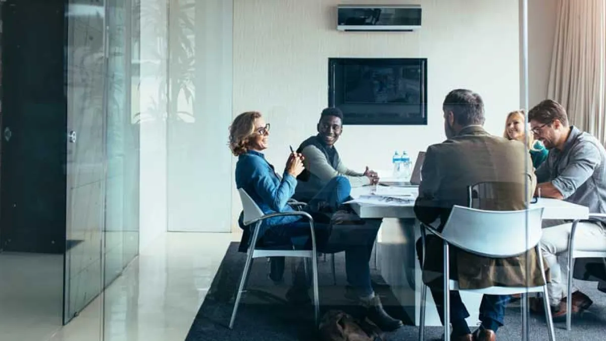 Four people sat round a table in a classroom environment, a glass screen to the left