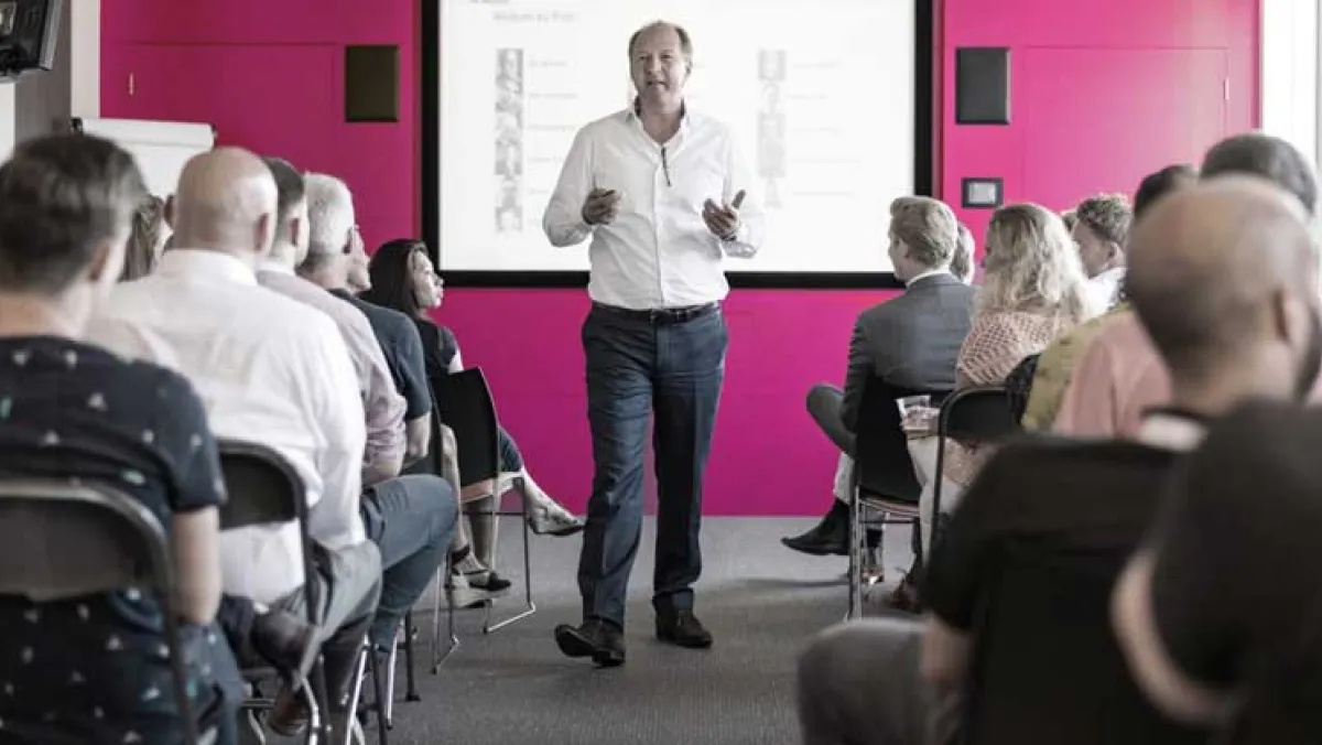 Man in a white shirt strolling through the centre column of a busy of classroom