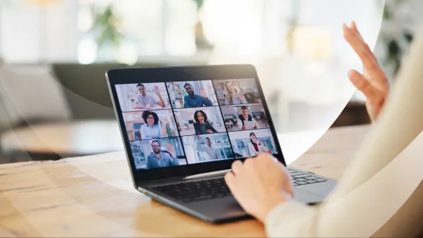 Person participating in an online video conference, engaging with multiple colleagues on a laptop screen.