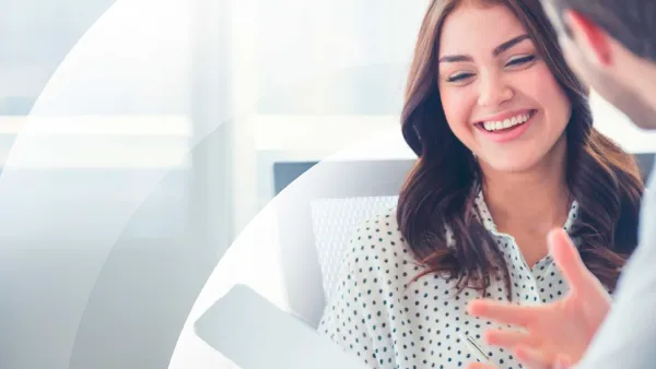 A woman smiling while talking with a colleague, holding a pen and document